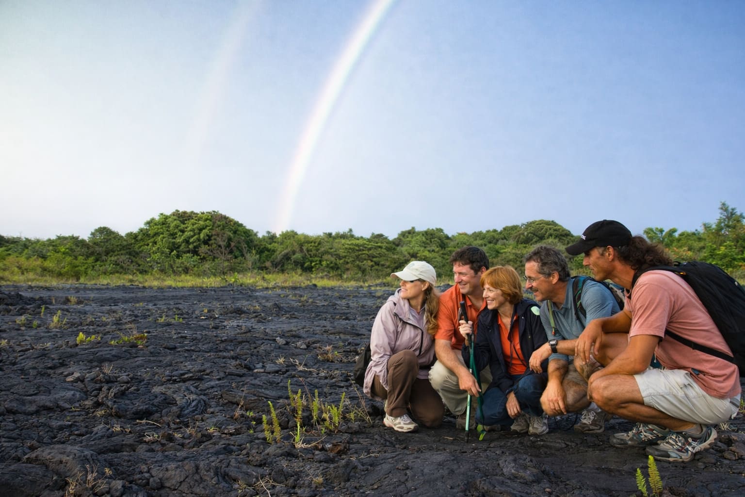 Visitors and a guide exploring a volcanic landscape beneath a rainbow